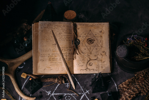 Open old book with magic spells, runes, black candles on witch table. Occult, esoteric, divination and wicca concept.