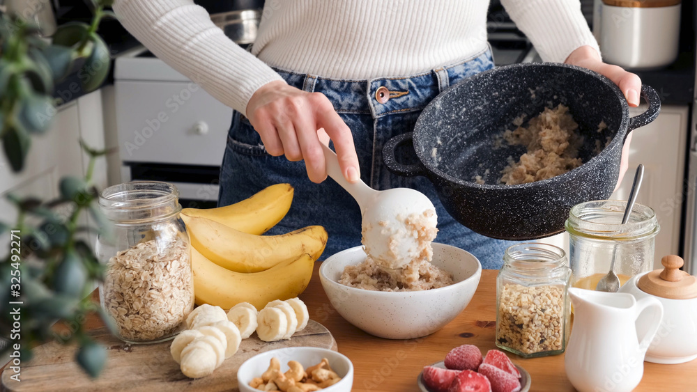 Fototapeta premium Woman putting oatmeal in a bowl with spoon. Preparing healthy breakfast at the kitchen. Healthy lifestyle concept