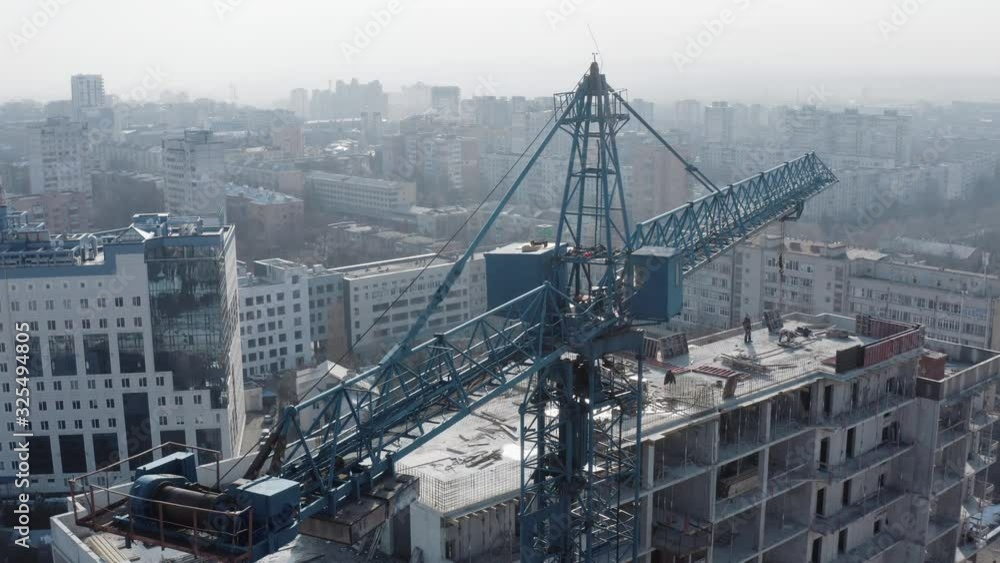 Circular top shot of the crane and the process of building a new multi-storey building in the winter season against the background of residential buildings. Workers on the roof are building a house. Circular top shot of the crane and the process of building a new multi-storey building in the winter season against the background of residential buildings. Workers on the roof are building a house.