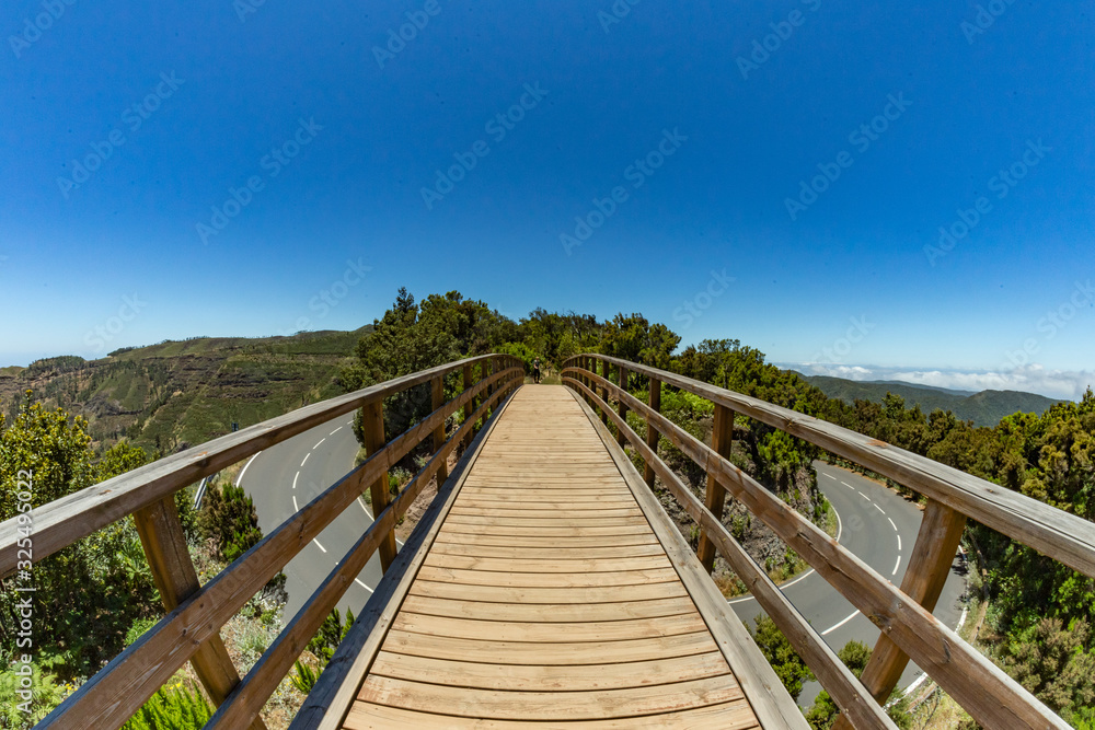 Pedestrian bridge across the main road. Relict forest on the slopes of the mountain range of the Garajonay National Park. Paradise for hiking. Fish eye lens shot. Travel postcard. La Gomera, Spain