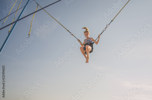 lovely blond caucasian girl jumping in the jump attraction in the playground