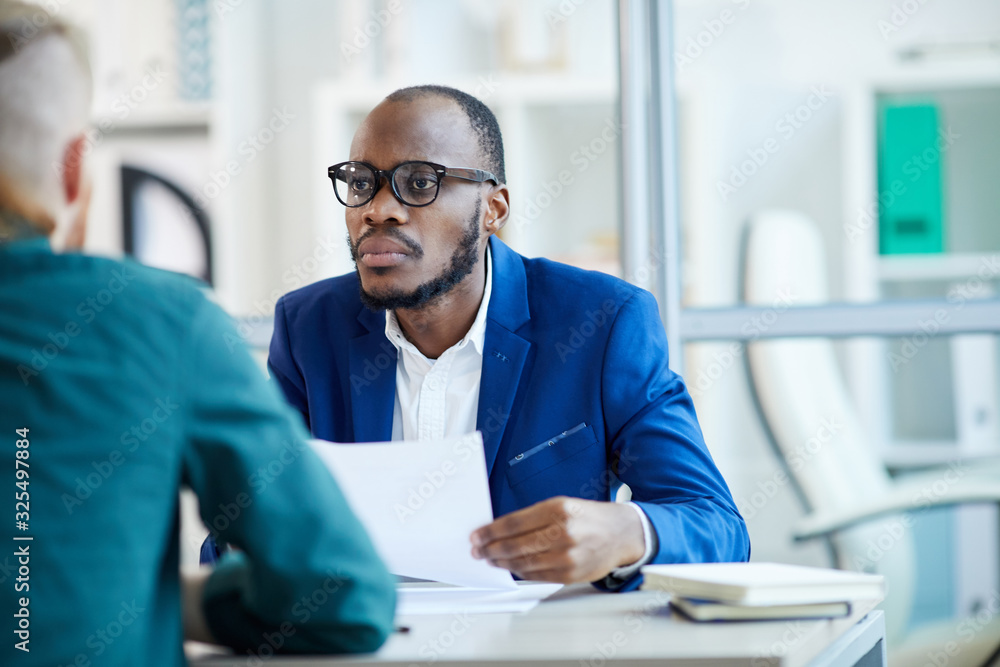 Fototapeta premium Portrait of contemporary African-American businessman listening to candidate during job interview in office, copy space