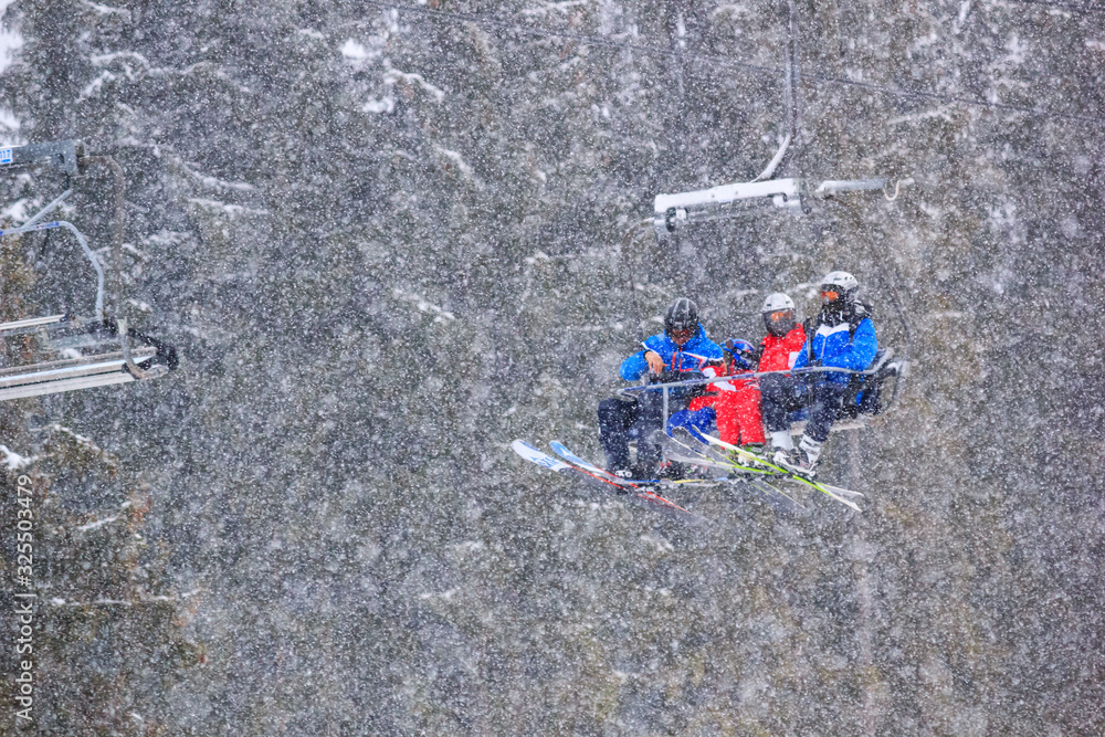 Winter landscape - view of the chairlift lift with skiers in the winter mountain forest during a snowfall, Bukovel ski resort, Carpathian mountains, Ukraine, 18 January, 2019 Winter landscape - view of the chairlift lift with skiers in the winter mountain forest during a snowfall, Bukovel ski resort, Carpathian mountains, Ukraine, 18 January, 2019