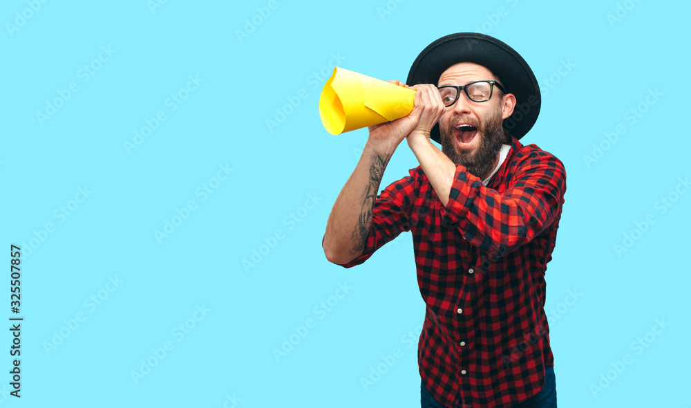 Handsome hipster guy wearing a red plaid shirt and hat looking through yellow rolled up paper as telescope. Your text here! Discount, sale, season sales. Handsome hipster guy wearing a red plaid shirt and hat looking through yellow rolled up paper as telescope. Your text here! Discount, sale, season sales.