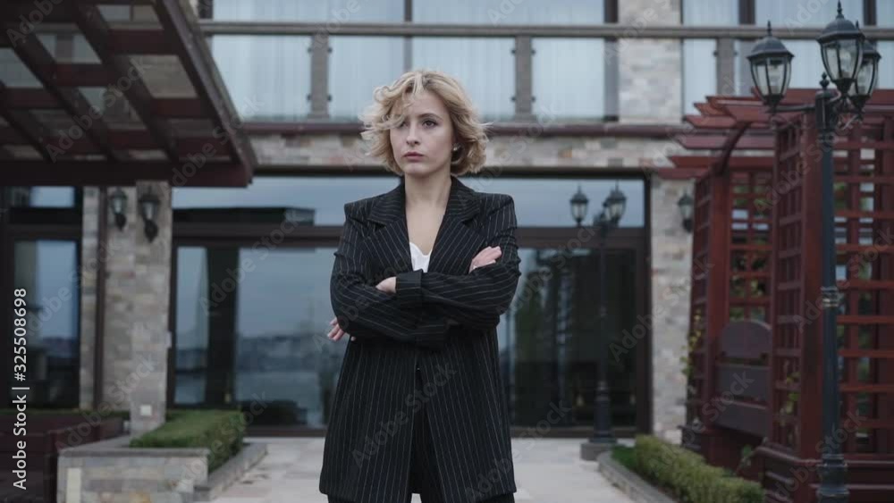 Stylish, thoughtful model in black suit stands in poses with crossed hands Stylish, thoughtful model in black suit stands in poses with crossed hands