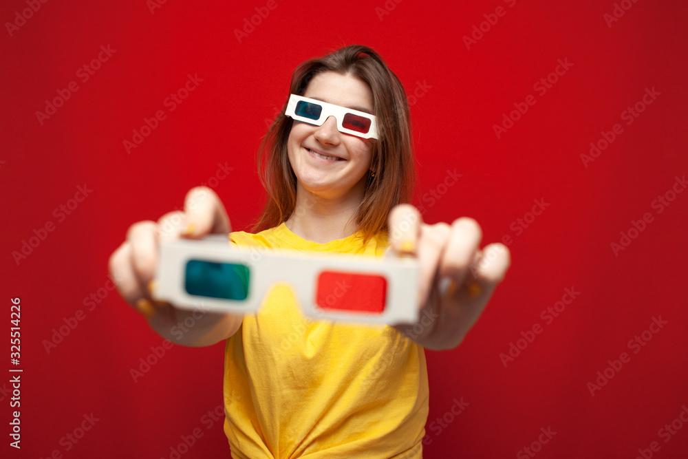 funny girl in 3D glasses on a red background gives glasses, offers to watch a movie funny girl in 3D glasses on a red background gives glasses, offers to watch a movie