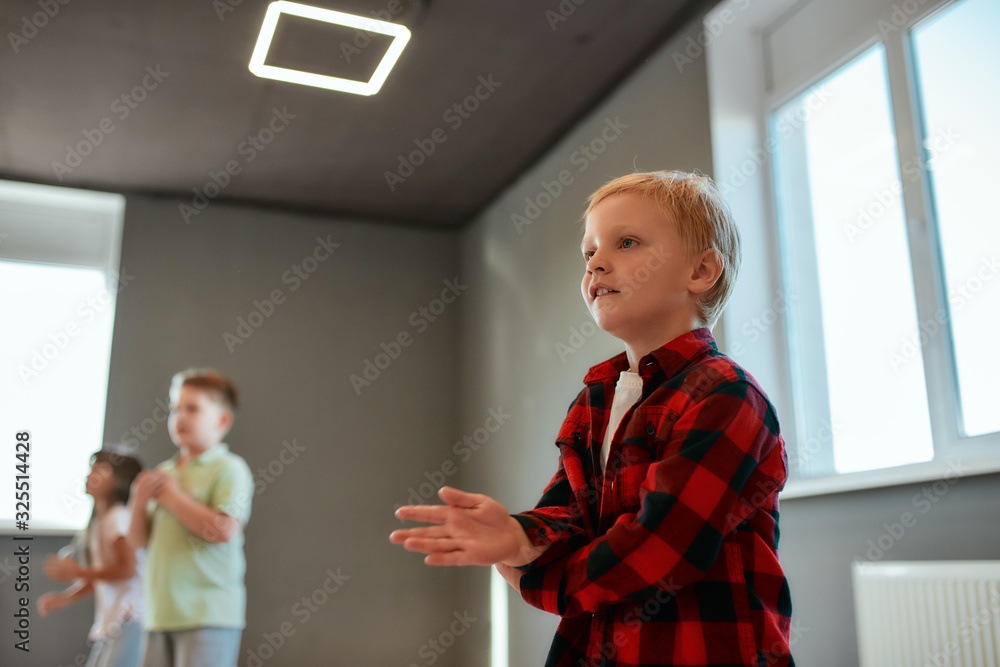 Cool dancer. Portrait of a little cute boy in checkered red shirt dancing while having a choreography class. Group of children studying in the dance school Cool dancer. Portrait of a little cute boy in checkered red shirt dancing while having a choreography class. Group of children studying in the dance school