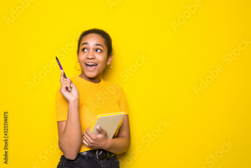 Young latin woman holding note book have idia isolated on yellow background