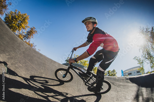 A young male riding a BMX bike through a berm while enjoying a sunny day. Low profile fisheye photo with sun in the background