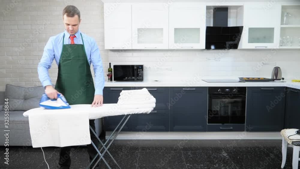 handsome man in a tie and apron ironing linen. cleaning concept handsome man in a tie and apron ironing linen. cleaning concept