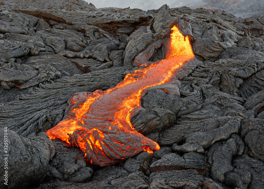 Hot magma of an active lava flow emerges from a fissure, the heat of