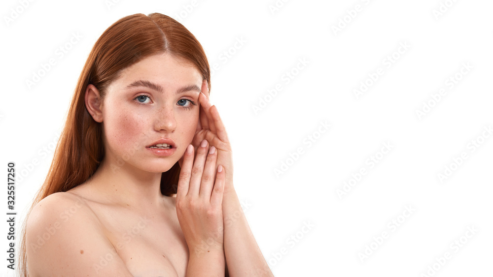 Fresh and clean. Portrait of a young sensual red-haired girl with freckles touching her face and looking at camera while standing against white background Fresh and clean. Portrait of a young sensual red-haired girl with freckles touching her face and looking at camera while standing against white background