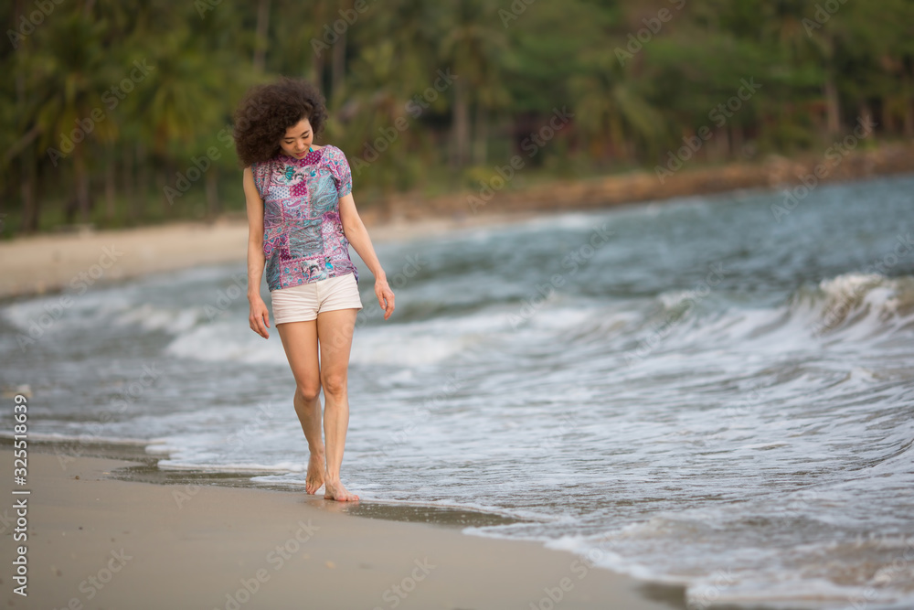 Woman of mixed race stands on the surf line on sea beach.