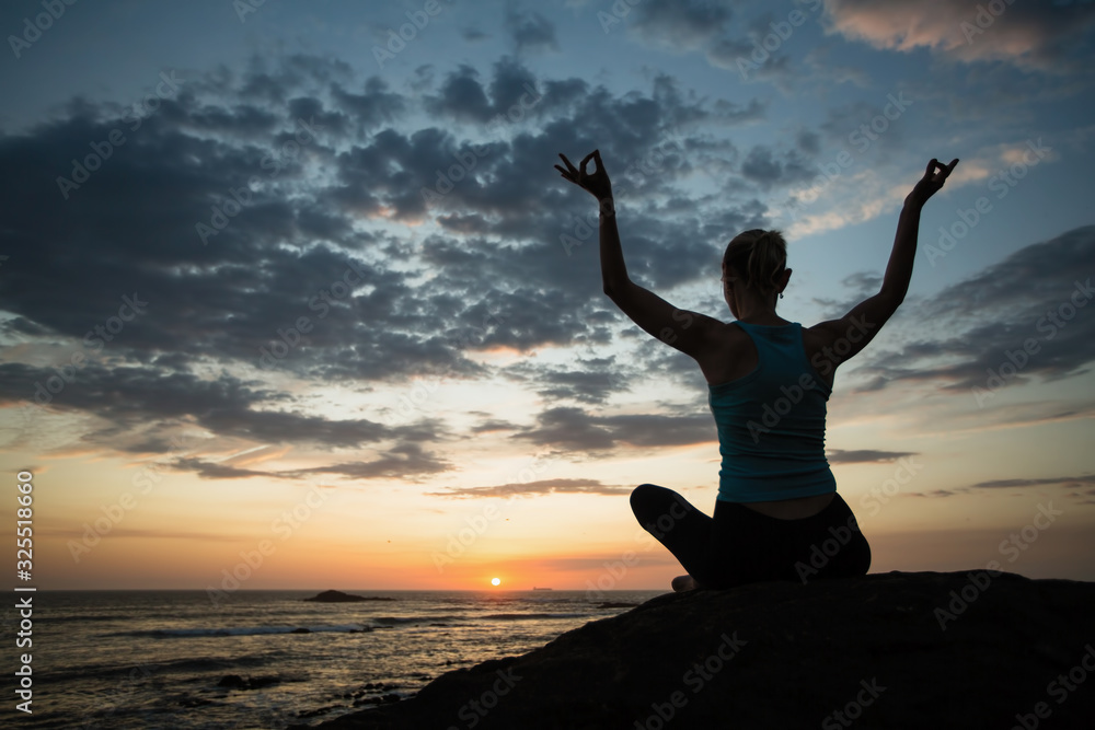 Yoga woman in lotus meditating on the ocean coast at dusk.