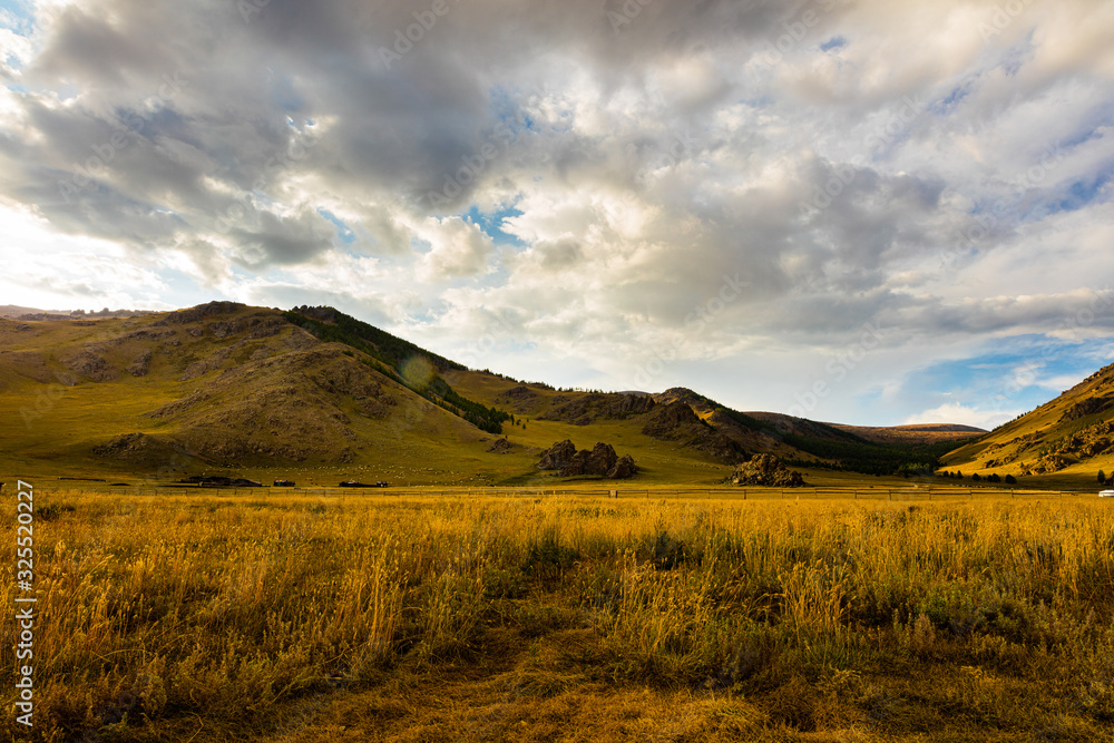 The sun goes down at Mongolia , Sunset Landscape photography in the Mongolian steppe at Arhangai-Aimag. Blue sky with white clouds and yellow steppe grass in foreground The sun goes down at Mongolia , Sunset Landscape photography in the Mongolian steppe at Arhangai-Aimag. Blue sky with white clouds and yellow steppe grass in foreground