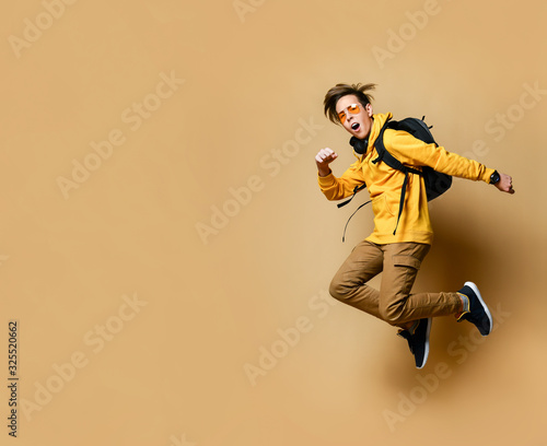 Portrait of a young student man jumping in the studio on a beige background