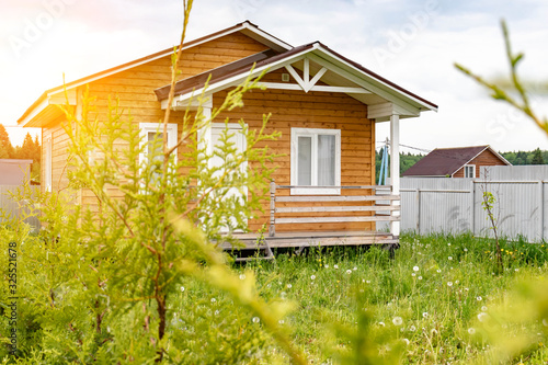 Small tiny wooden frame house with sundeck and white windows and door as a country residence in sunny summer day