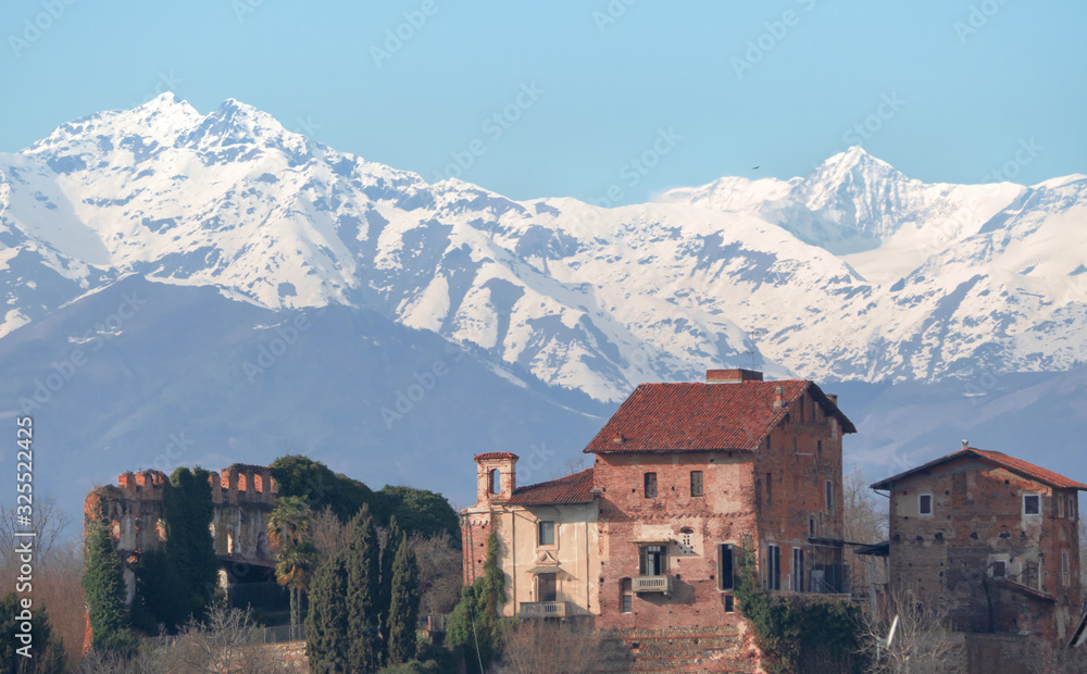 ancient country cottage on the top of a hill with snow-capped mountains and blue skies in the background.Biella,Piedmont,Italy.