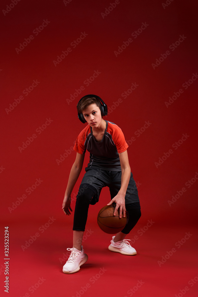 Take it to the Net. A teenage boy is engaged in sport, looking at camera while exercising with basketball. Isolated on red background. Fitness, training, active lifestyle concept. Vertical shot.