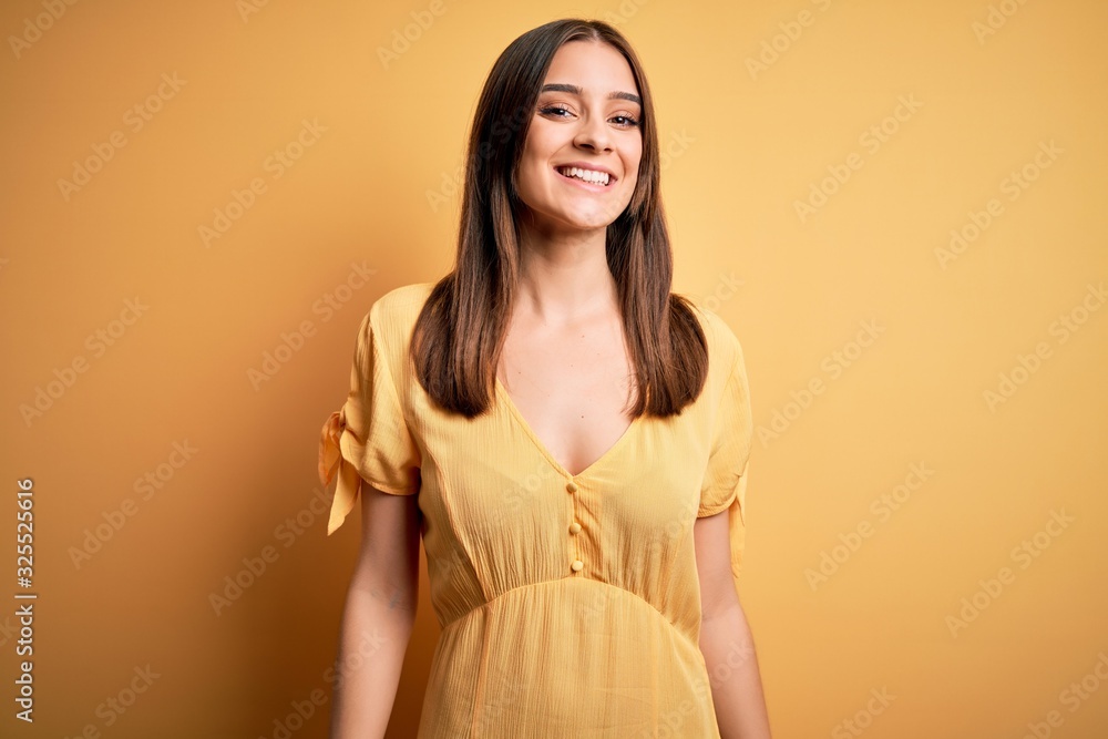 Obraz premium Young beautiful brunette woman wearing casual dress standing over yellow background with a happy and cool smile on face. Lucky person.