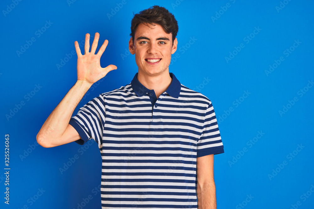 Teenager boy wearing casual t-shirt standing over blue isolated background showing and pointing up with fingers number five while smiling confident and happy. Teenager boy wearing casual t-shirt standing over blue isolated background showing and pointing up with fingers number five while smiling confident and happy.