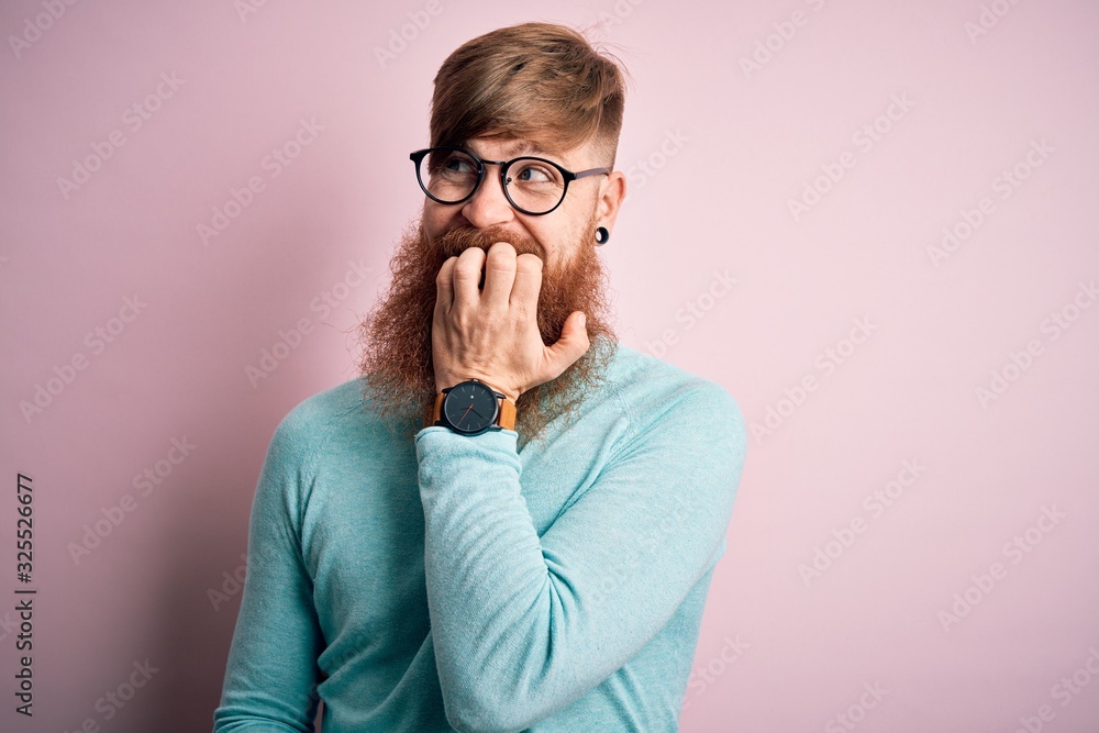 Handsome Irish redhead man with beard wearing glasses over pink isolated background looking stressed and nervous with hands on mouth biting nails. Anxiety problem. Handsome Irish redhead man with beard wearing glasses over pink isolated background looking stressed and nervous with hands on mouth biting nails. Anxiety problem.