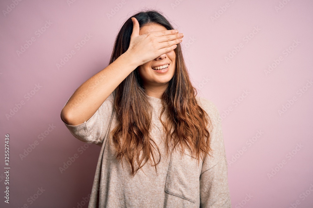 Young beautiful brunette woman wearing casual sweater standing over pink background smiling and laughing with hand on face covering eyes for surprise. Blind concept. Young beautiful brunette woman wearing casual sweater standing over pink background smiling and laughing with hand on face covering eyes for surprise. Blind concept.