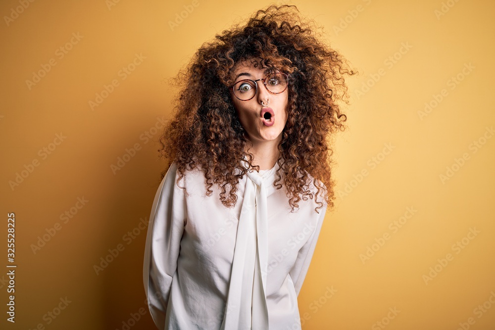 Young beautiful brunette woman with curly hair and piercing wearing shirt and glasses afraid and shocked with surprise expression, fear and excited face. Young beautiful brunette woman with curly hair and piercing wearing shirt and glasses afraid and shocked with surprise expression, fear and excited face.
