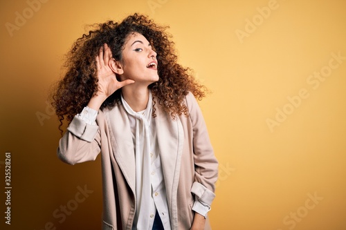 Young beautiful brunette woman with curly hair and piercing wearing casual t-shirt and diadem smiling with hand over ear listening an hearing to rumor or gossip. Deafness concept.