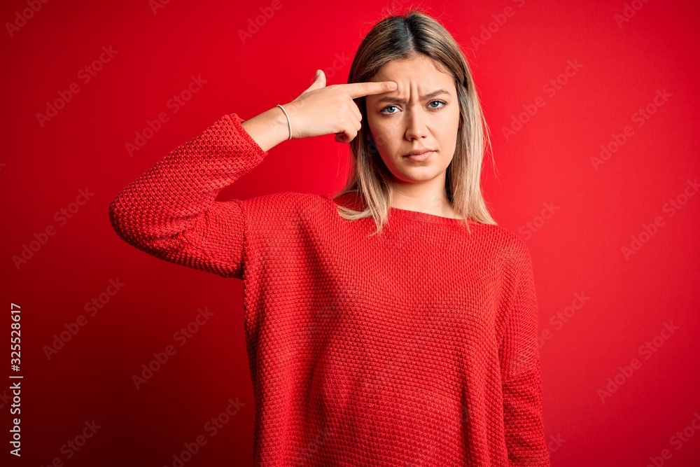 Young beautiful blonde woman wearing casual sweater over red isolated background pointing unhappy to pimple on forehead, ugly infection of blackhead. Acne and skin problem Young beautiful blonde woman wearing casual sweater over red isolated background pointing unhappy to pimple on forehead, ugly infection of blackhead. Acne and skin problem
