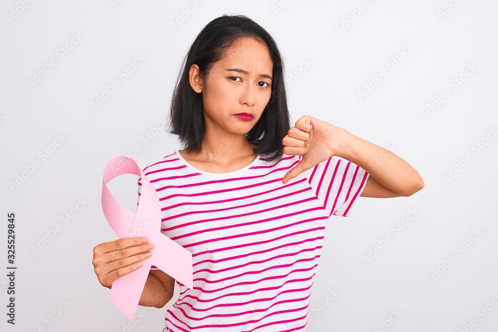 Young beautiful chinese woman holding cancer ribbon over isolated white background with angry face, negative sign showing dislike with thumbs down, rejection concept Young beautiful chinese woman holding cancer ribbon over isolated white background with angry face, negative sign showing dislike with thumbs down, rejection concept