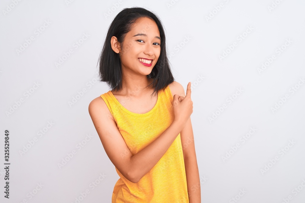 Young chinese woman wearing yellow casual t-shirt standing over isolated white background cheerful with a smile of face pointing with hand and finger up to the side with happy and natural expression Young chinese woman wearing yellow casual t-shirt standing over isolated white background cheerful with a smile of face pointing with hand and finger up to the side with happy and natural expression