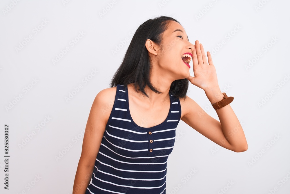 Young chinese woman wearing striped t-shirt standing over isolated white background shouting and screaming loud to side with hand on mouth. Communication concept. Young chinese woman wearing striped t-shirt standing over isolated white background shouting and screaming loud to side with hand on mouth. Communication concept.