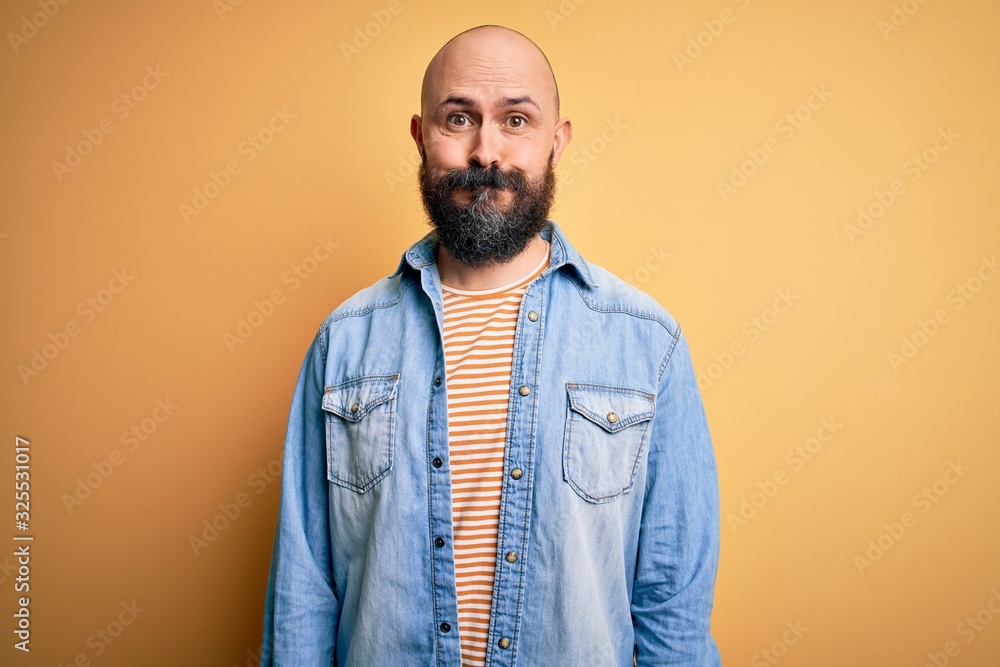 Handsome bald man with beard wearing casual denim jacket and striped t-shirt puffing cheeks with funny face. Mouth inflated with air, crazy expression. Handsome bald man with beard wearing casual denim jacket and striped t-shirt puffing cheeks with funny face. Mouth inflated with air, crazy expression.