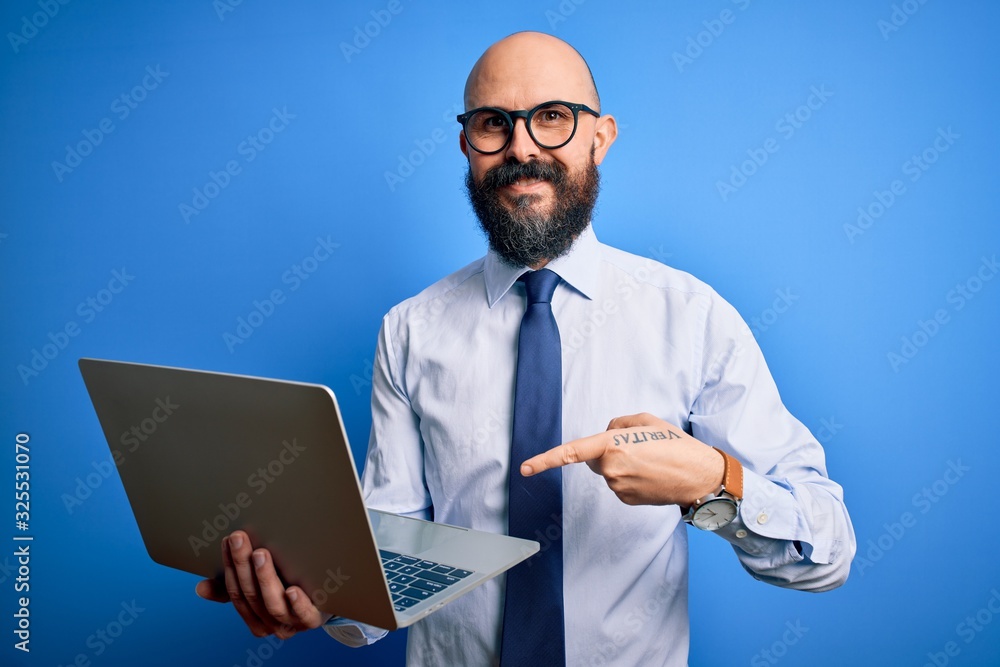 Handsome bald business man with beard working using laptop over blue background very happy pointing with hand and finger Handsome bald business man with beard working using laptop over blue background very happy pointing with hand and finger