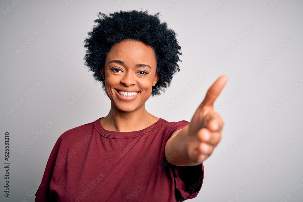 Young beautiful African American afro woman with curly hair wearing casual t-shirt standing smiling friendly offering handshake as greeting and welcoming. Successful business. Young beautiful African American afro woman with curly hair wearing casual t-shirt standing smiling friendly offering handshake as greeting and welcoming. Successful business.