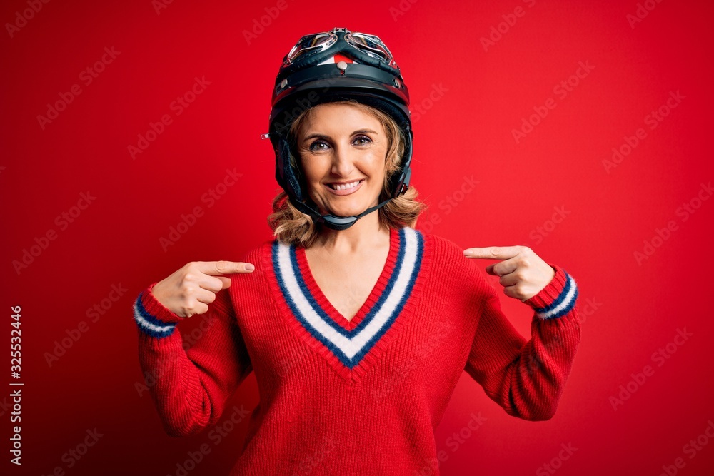 Middle age beautiful blonde motorcyclist woman wearing moto helmet over red background looking confident with smile on face, pointing oneself with fingers proud and happy. Middle age beautiful blonde motorcyclist woman wearing moto helmet over red background looking confident with smile on face, pointing oneself with fingers proud and happy.
