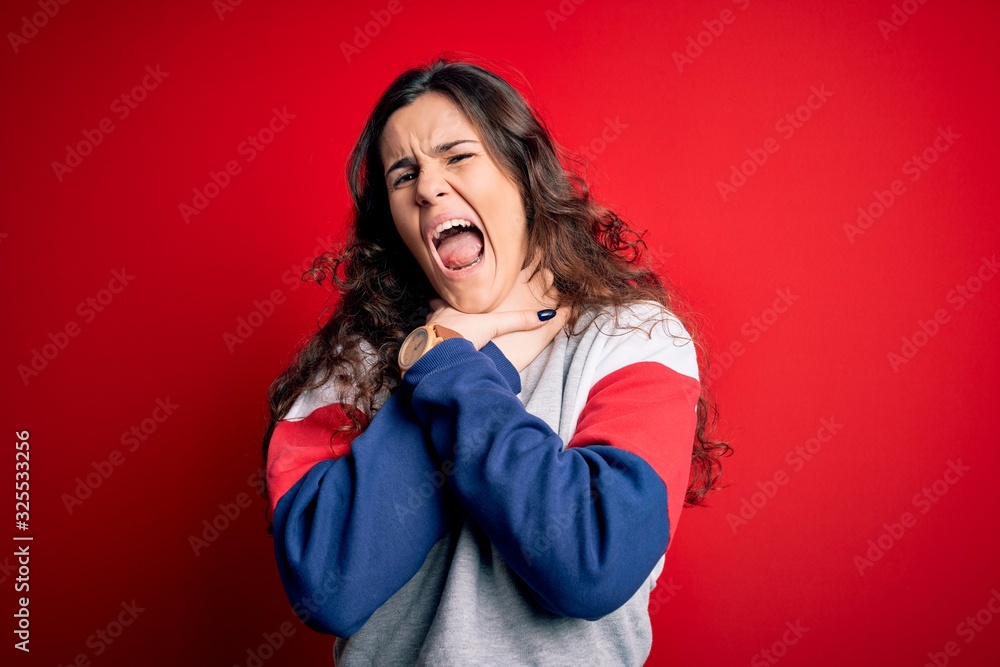 Young beautiful woman with curly hair wearing casual sweatshirt over isolated red background shouting suffocate because painful strangle. Health problem. Asphyxiate and suicide concept. Young beautiful woman with curly hair wearing casual sweatshirt over isolated red background shouting suffocate because painful strangle. Health problem. Asphyxiate and suicide concept.