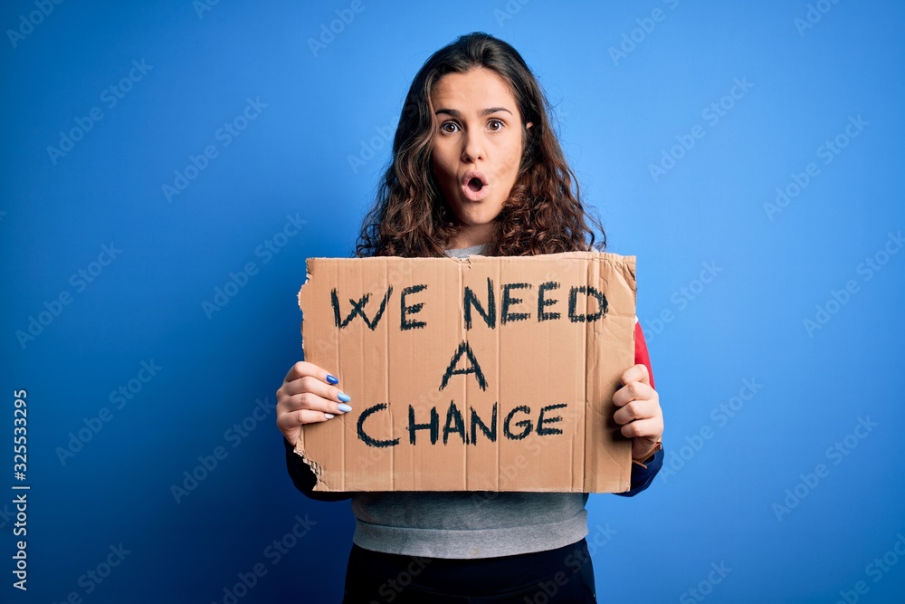 Young beautiful activist woman holding banner with change message over blue background scared in shock with a surprise face, afraid and excited with fear expression Young beautiful activist woman holding banner with change message over blue background scared in shock with a surprise face, afraid and excited with fear expression