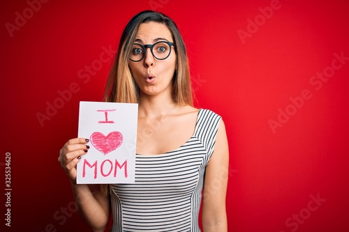 Young beautiful woman holding paper with love mom message celebrating mothers day scared in shock with a surprise face, afraid and excited with fear expression