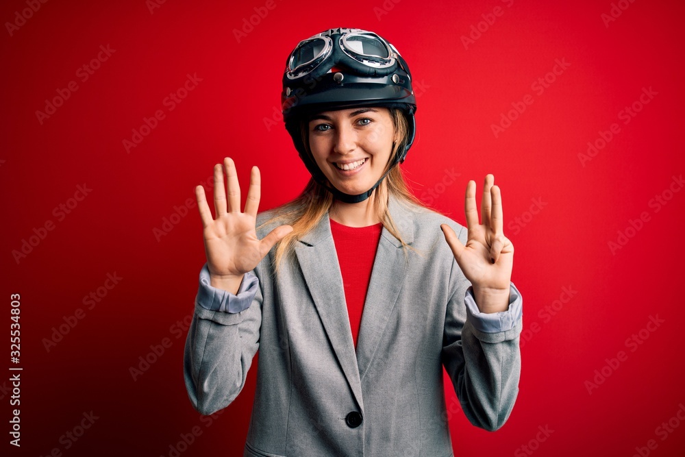 Young beautiful blonde motorcyclist woman wearing motorcycle helmet over red background showing and pointing up with fingers number nine while smiling confident and happy.