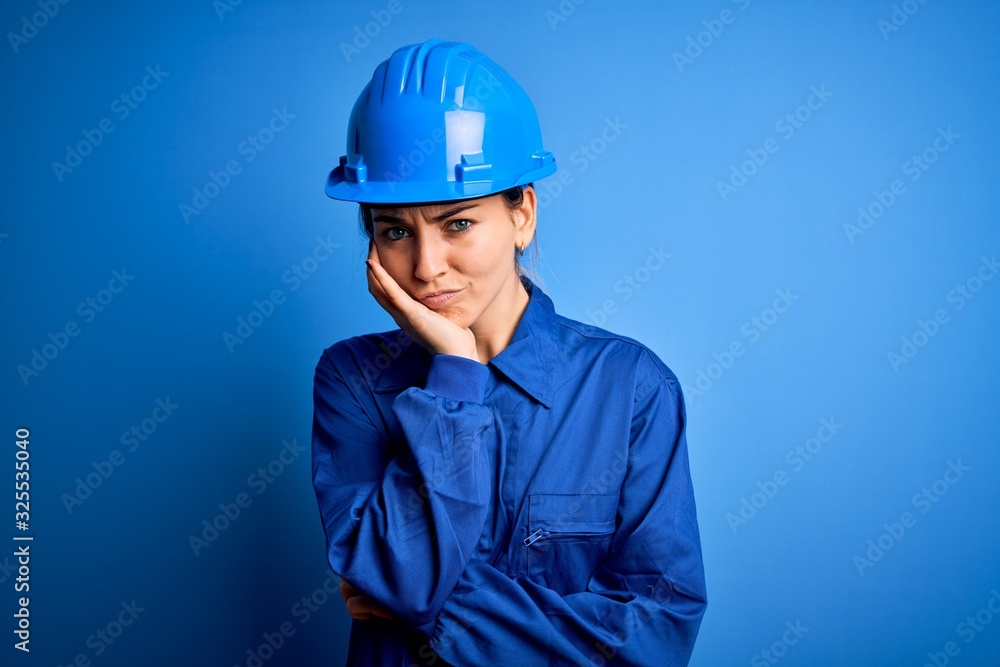 Young beautiful worker woman with blue eyes wearing security helmet and uniform thinking looking tired and bored with depression problems with crossed arms.