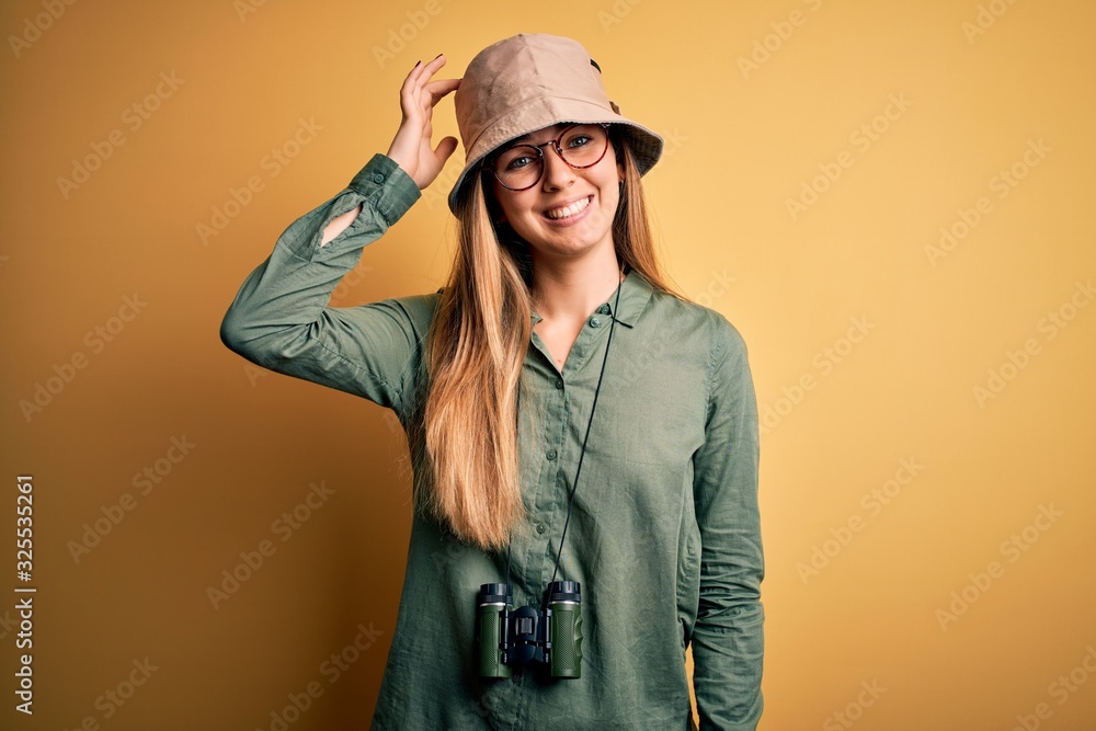 Beautiful blonde explorer woman with blue eyes wearing hat and glasses using binoculars confuse and wonder about question. Uncertain with doubt, thinking with hand on head. Pensive concept. Beautiful blonde explorer woman with blue eyes wearing hat and glasses using binoculars confuse and wonder about question. Uncertain with doubt, thinking with hand on head. Pensive concept.