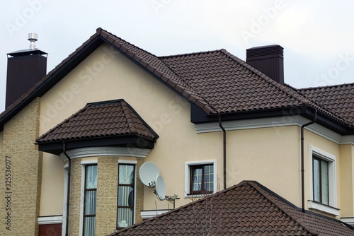 part of a brown house with windows on the wall under a tiled roof 