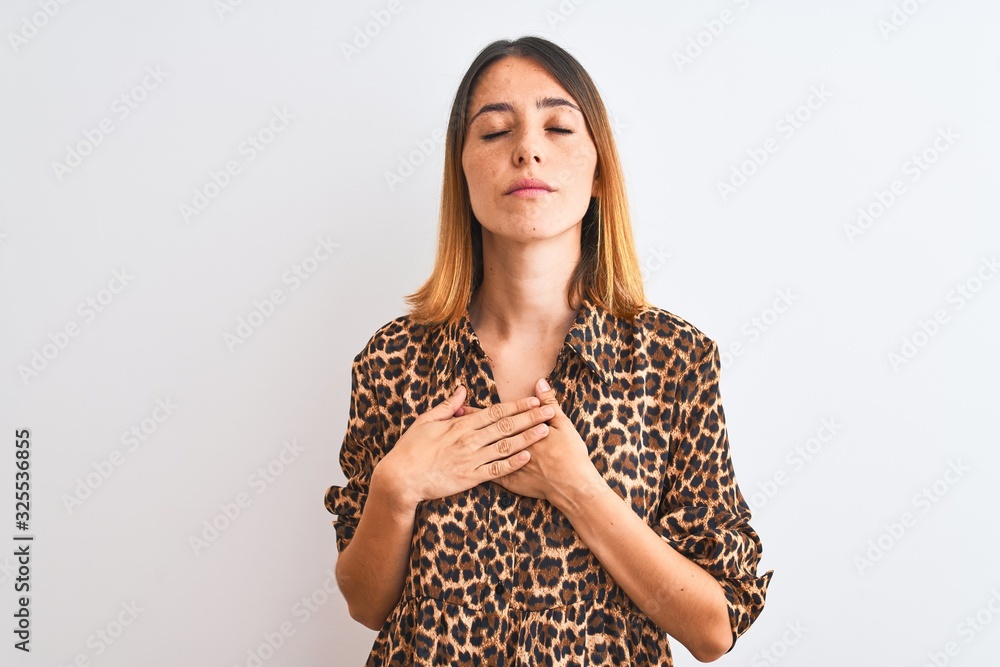 Beautiful redhead woman wearing elegant animal print shirt over isolated background smiling with hands on chest with closed eyes and grateful gesture on face. Health concept. Beautiful redhead woman wearing elegant animal print shirt over isolated background smiling with hands on chest with closed eyes and grateful gesture on face. Health concept.