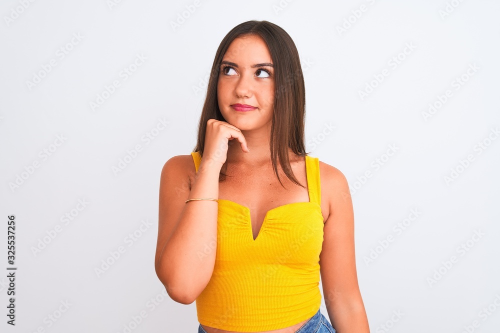 Young beautiful girl wearing yellow casual t-shirt standing over isolated white background with hand on chin thinking about question, pensive expression. Smiling with thoughtful face. Doubt concept. Young beautiful girl wearing yellow casual t-shirt standing over isolated white background with hand on chin thinking about question, pensive expression. Smiling with thoughtful face. Doubt concept.