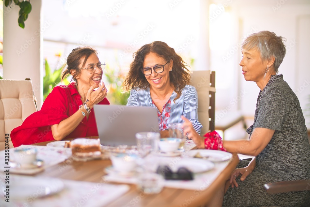 Meeting of middle age women having lunch and drinking coffee. Mature friends smiling happy using laptop at home on a sunny day Meeting of middle age women having lunch and drinking coffee. Mature friends smiling happy using laptop at home on a sunny day