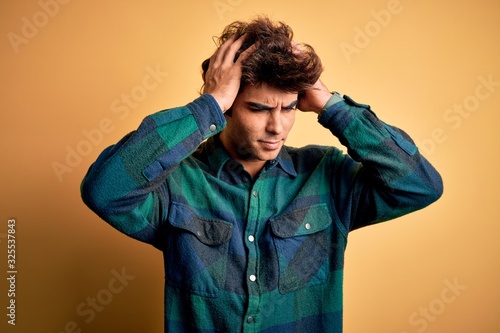 Young handsome man wearing casual shirt standing over isolated yellow background suffering from headache desperate and stressed because pain and migraine. Hands on head. © Krakenimages.com