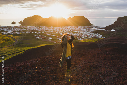 Young happy woman enjoying sunset on peak of Eldfell volcano with panoramic view of Vestmannaeyjar island in Iceland. Wanderlust travel concept. Amazing colorful sunset. photo