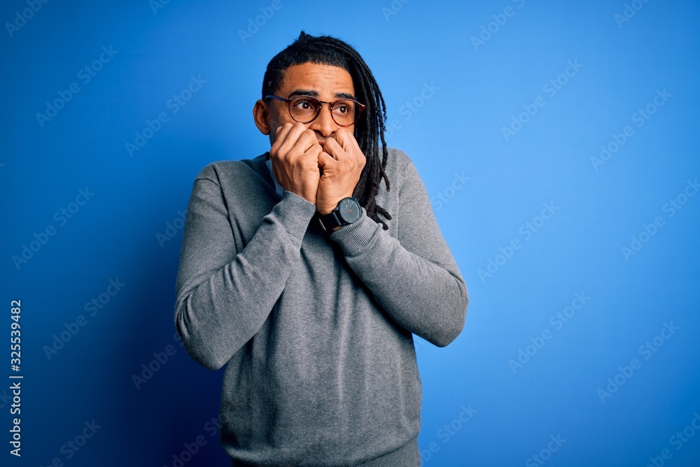 Young handsome african american man with dreadlocks wearing casual sweater and glasses looking stressed and nervous with hands on mouth biting nails. Anxiety problem. Young handsome african american man with dreadlocks wearing casual sweater and glasses looking stressed and nervous with hands on mouth biting nails. Anxiety problem.